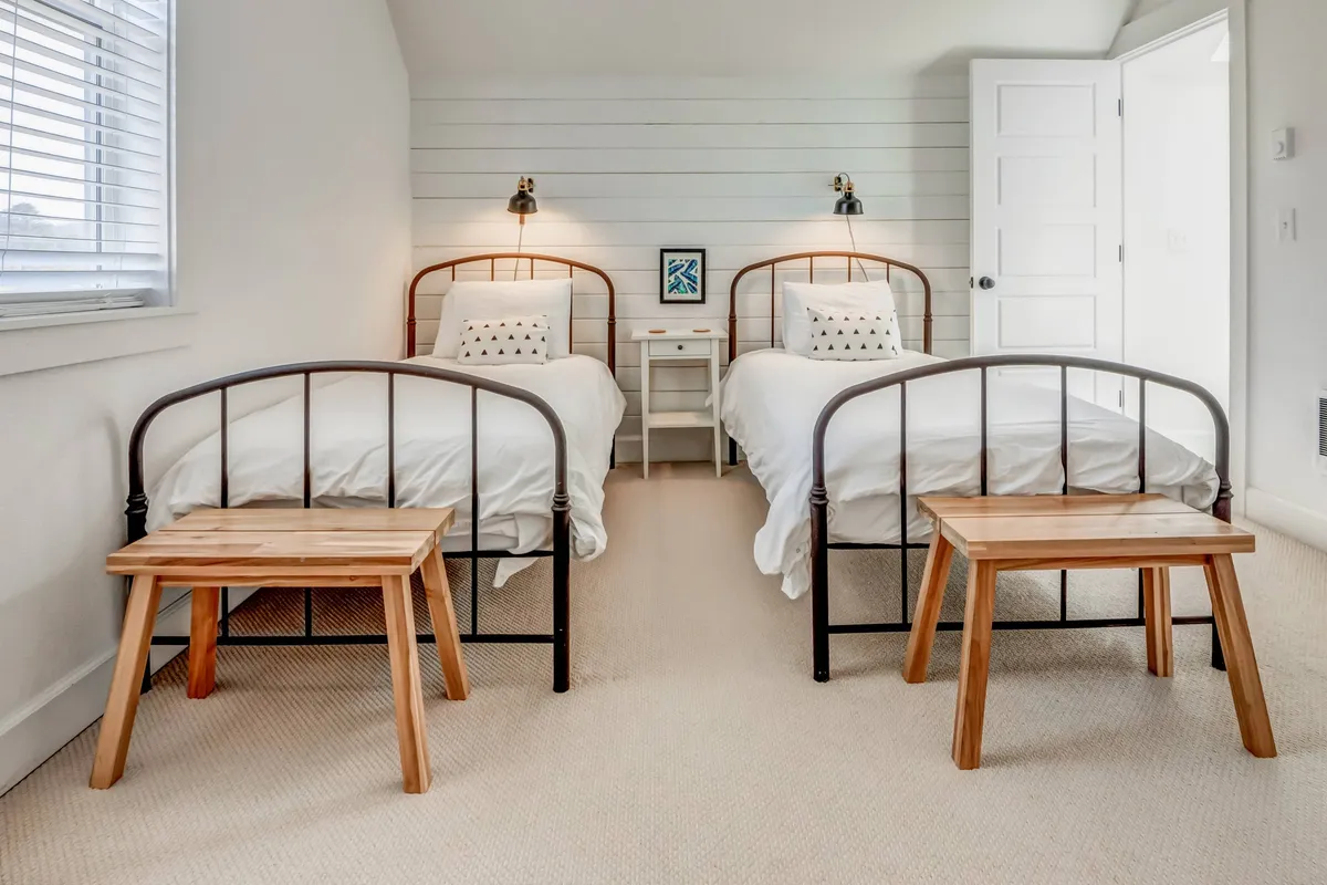 A cozy bedroom with two beds, a nightstand, and attractive wall art. The soft bedding and coordinated decor suggest a comfortable atmosphere for families or groups, offering flexibility in sleeping arrangements.