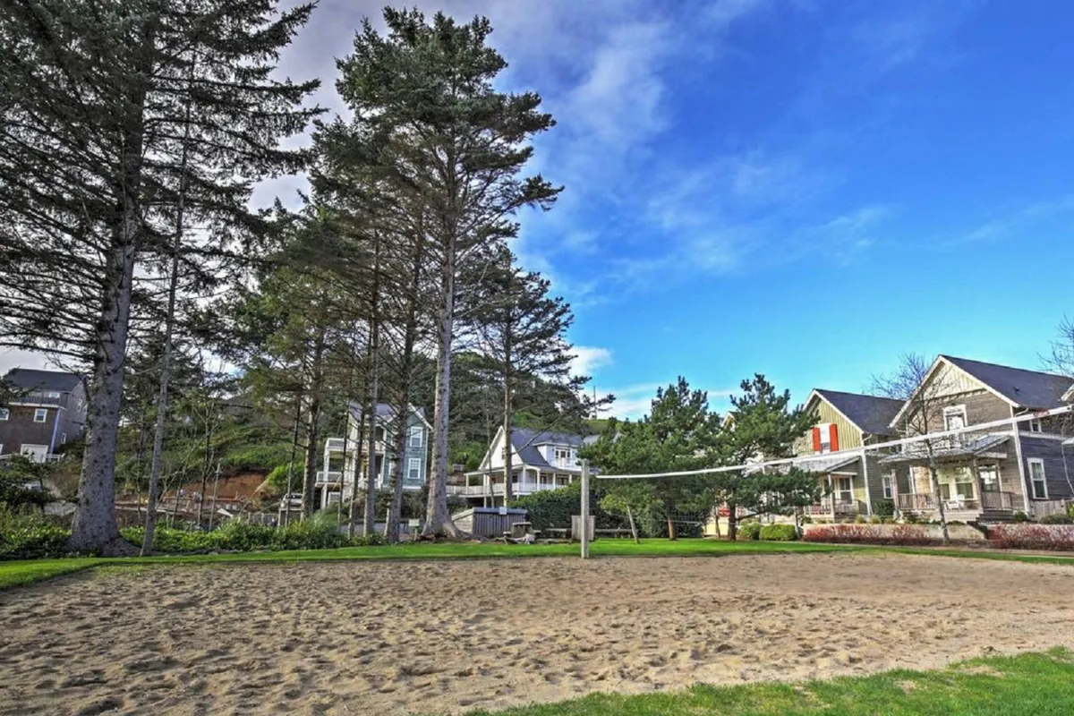 The image captures a lively sand volleyball court surrounded by tall trees and neighboring homes, with groups of people playing volleyball and others relaxing nearby. The energy of community gatherings underlines the shared amenities aspect of the property.