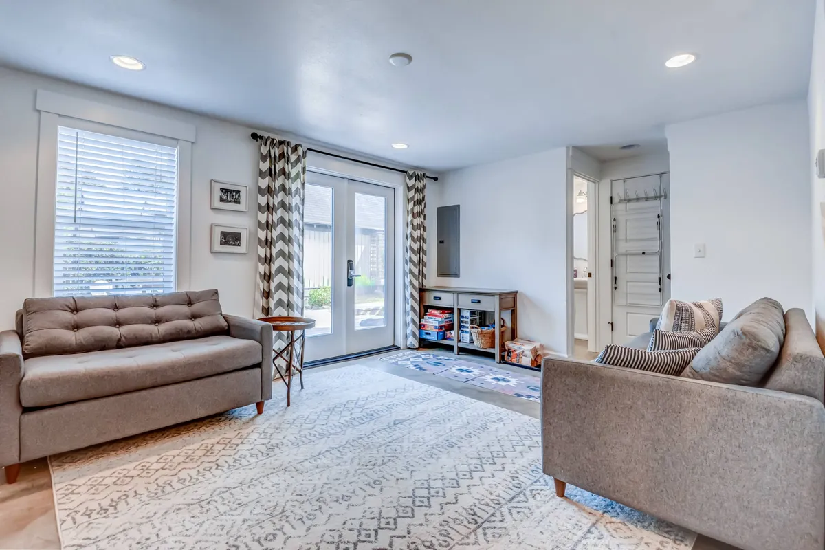 This interior image showcases a comfortable sofa positioned on a stylish rug, with French doors letting in abundant daylight and decorative curtains framing the view. A side table adds to the cozy, inviting vibe, perfect for lounging, reading, or socializing.