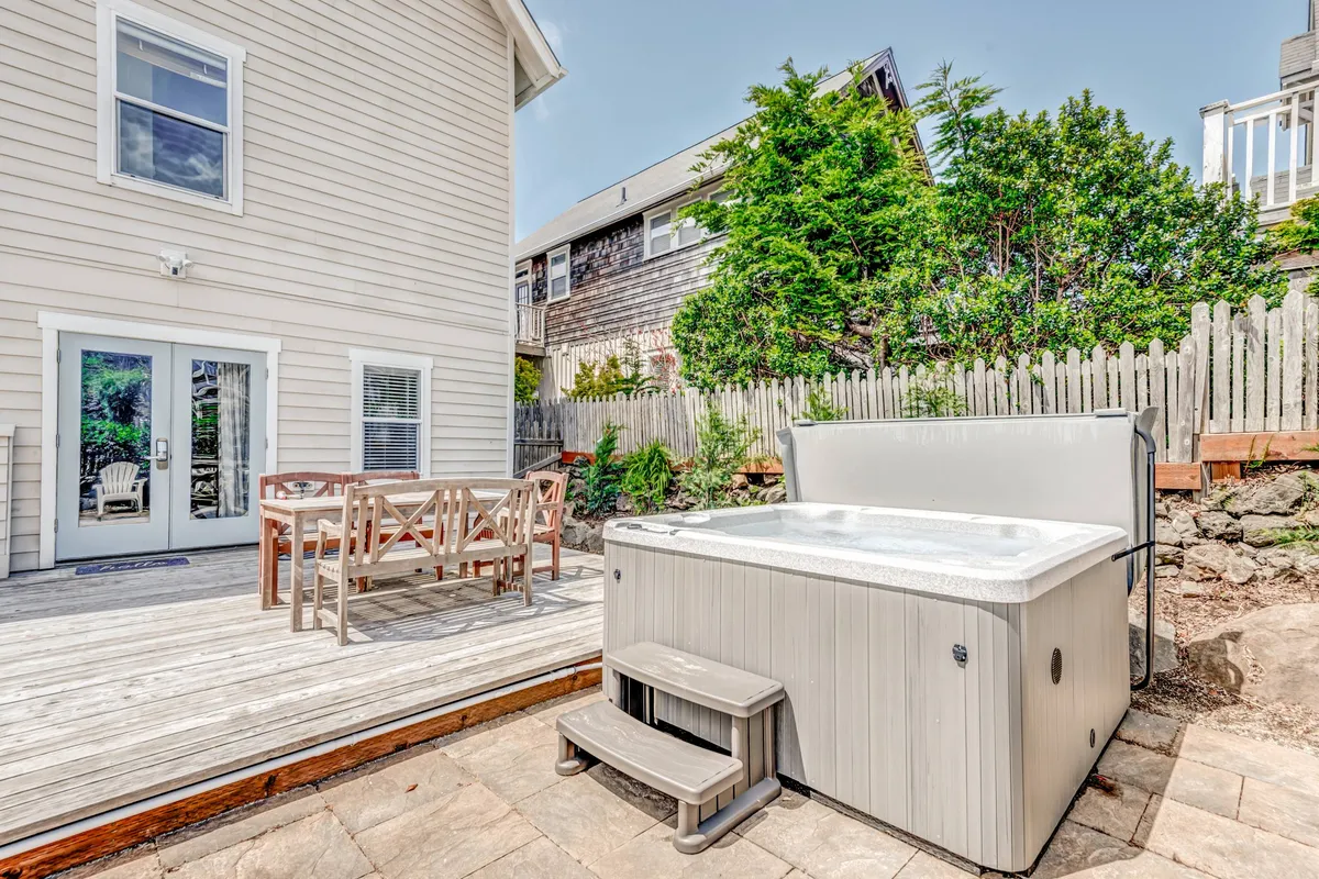 A serene deck set amidst lush garden greenery, showcasing a hot tub, outdoor dining table, and tranquil setting ideal for gatherings or quiet evenings under the stars.
