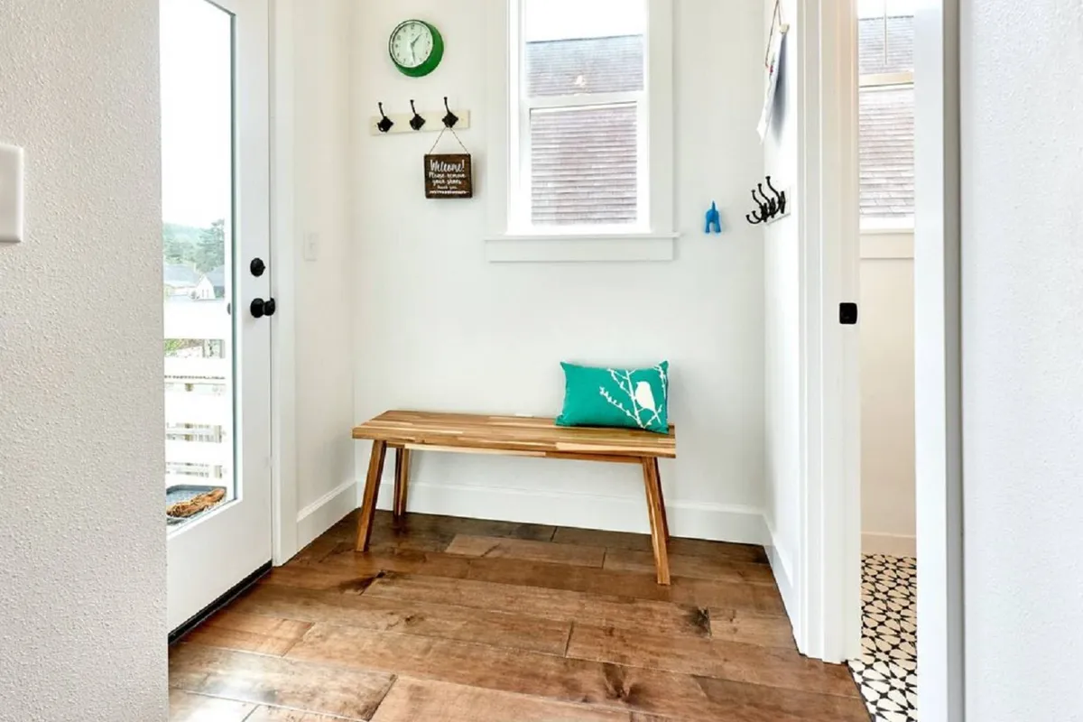 This image features a welcoming entrance area with a wooden bench, green cushion, wall clock, and hooks for coats. The space is inviting and serves as a transition zone between the outdoors and the home's interior, hinting at comings and goings for shopping, dining, or exploring the city.