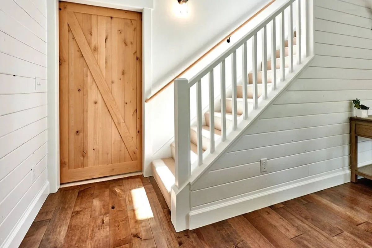 An inviting entryway featuring a wooden door, a staircase, and a welcoming side table. The space hints at transitions—moving from indoors out, or vice versa—suggesting ease of access for quick beach breaks or trips to nearby amenities.