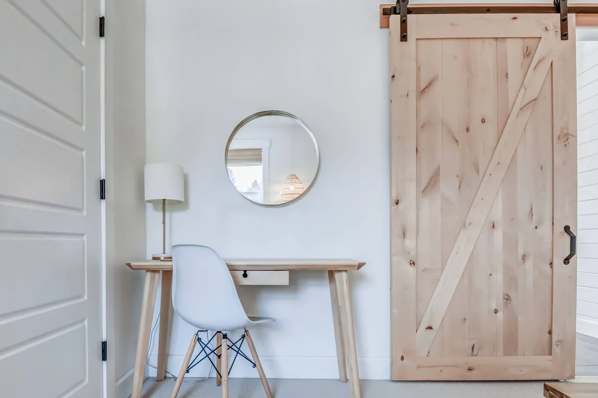 A quiet, minimalist workspace featuring a wooden sliding door, a modern desk with a comfortable chair, and a round mirror. The space is bathed in gentle natural light, creating a serene environment ideal for focused work or creative inspiration.