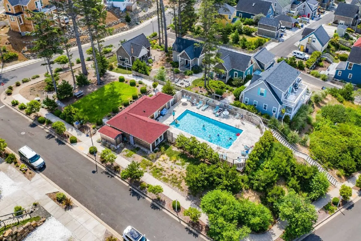 A seasonal heated swimming pool surrounded by greenery and a red-roofed building, with neighboring homes nearby. The pool area is designed for lounging, sunbathing, and playful moments with family and friends.