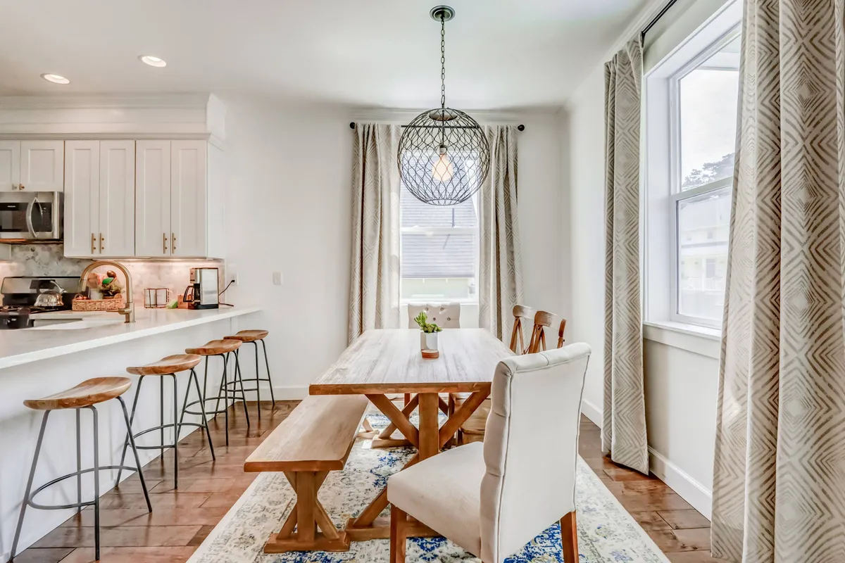 A warm, spacious dining area with a prominent dining table, chandelier, bar stools, and a window with curtains. The area is ideal for group meals, family gatherings, and socializing after a day out.
