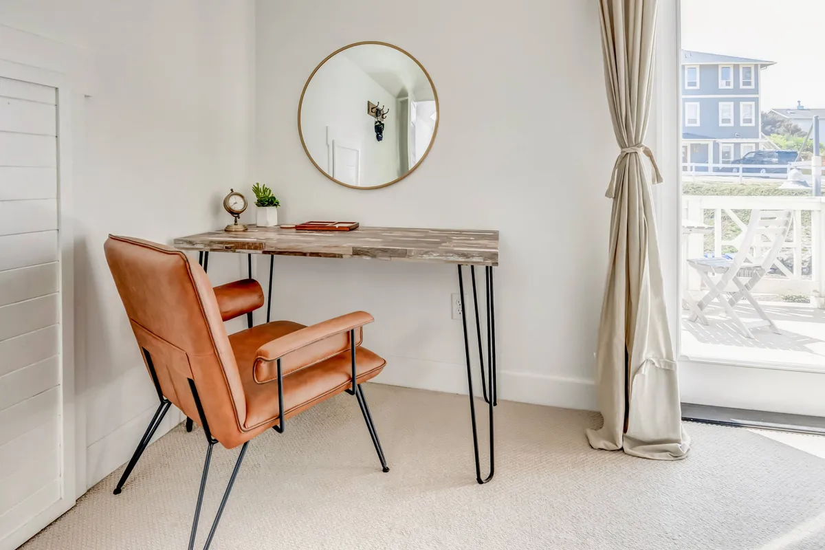 A productive nook with a modern desk and chair placed by a window, accompanied by a mirror. The setup suggests a quiet atmosphere perfect for reading, reflecting, or tackling work tasks with a view outside.
