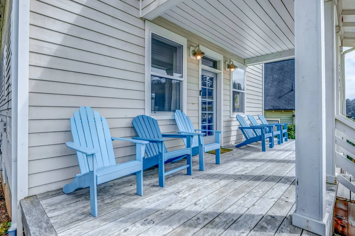 This image captures a tranquil outdoor porch with blue Adirondack chairs, a wooden surface, and windows glowing with natural light. It suggests a welcoming, pet-friendly environment where guests can enjoy quiet moments outdoors, perhaps after a walk with their pets.